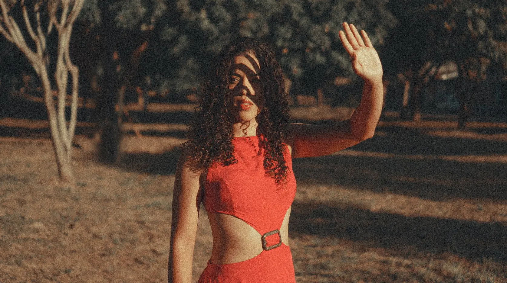 Modelo de vestido vermelho acenando em ensaio fotográfico ao entardecer