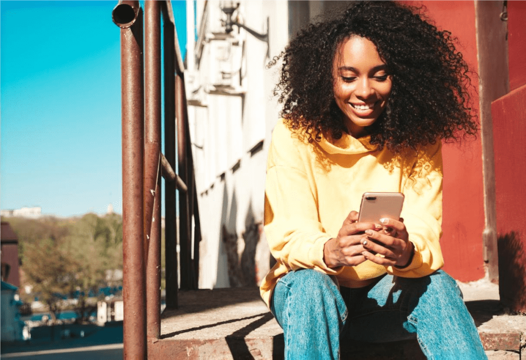 Mulher negra sorrindo para a tela do celular