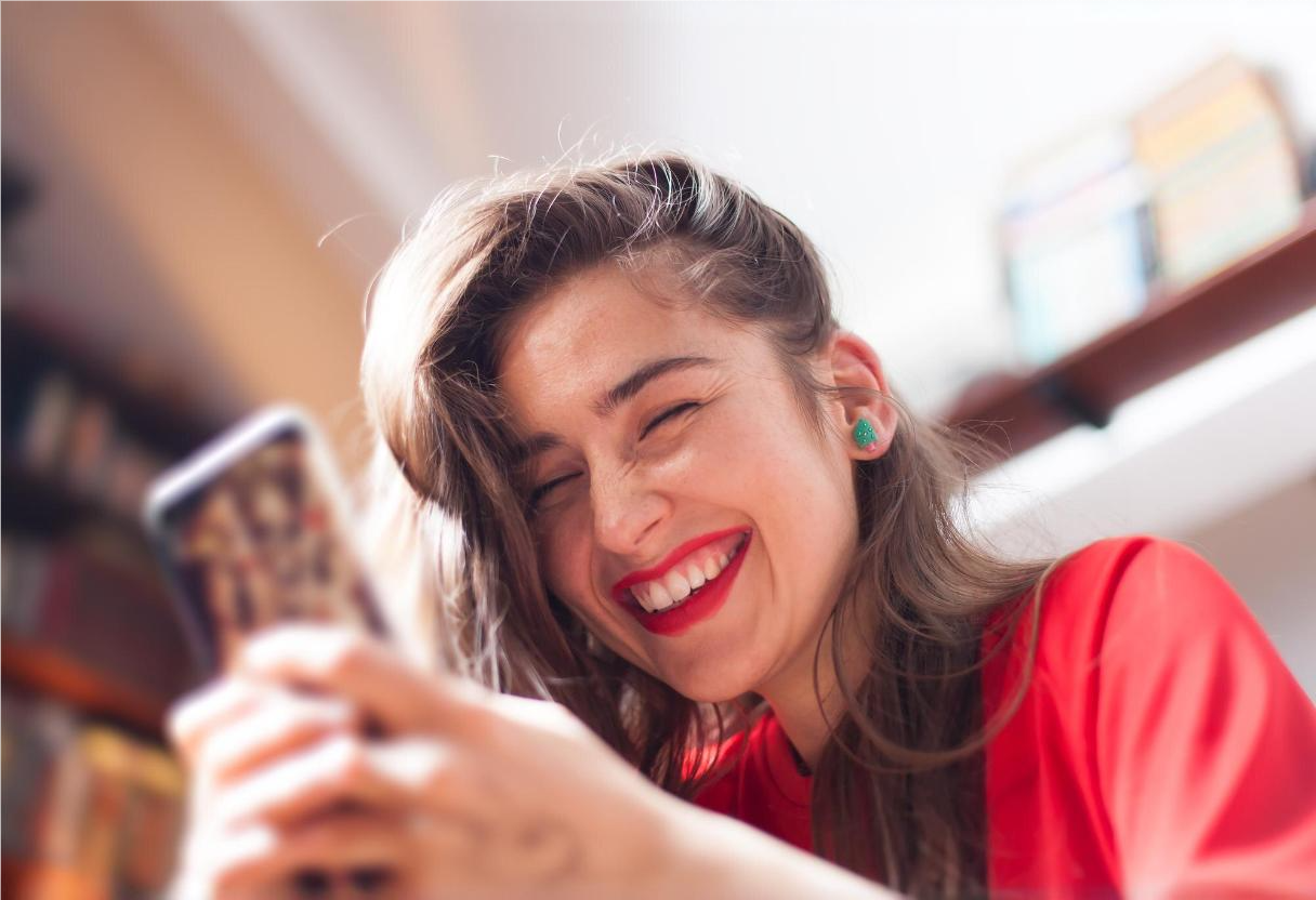 Mulher sorrindo para o celular ao verificar trending topics