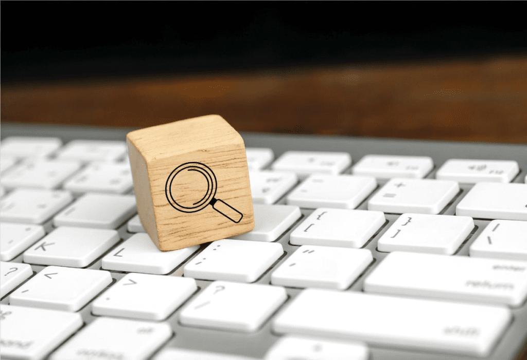 Cubo de madeira estampado com lupa sobre teclado de computador, representando o SEO